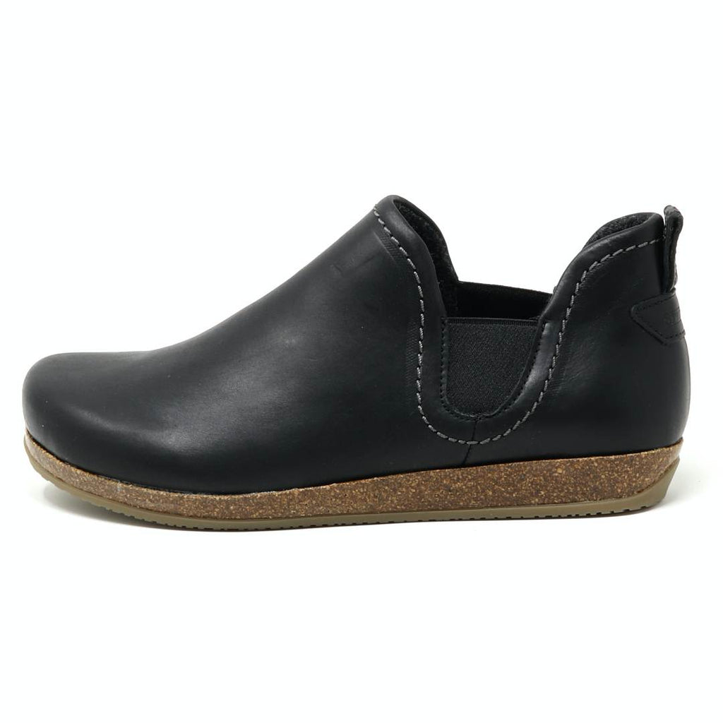 The Women's Lieben Leather Chelsea Boot is a black slip-on featuring a wool felt lining, brown cork sole, and white stitching, viewed from the side.